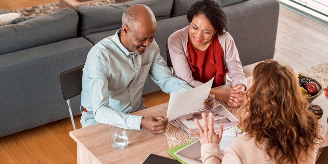 Photograph of a meeting between three adults to review paperwork while sitting at a kitchen table.